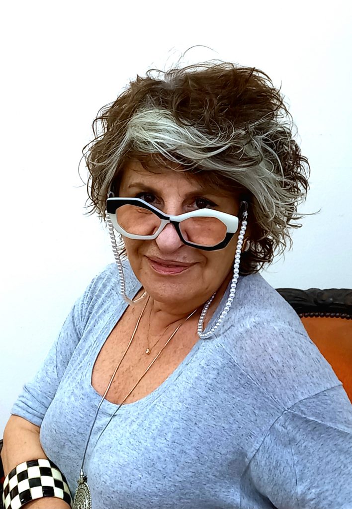 a foto mostra uma mulher com cabelo curto, óculos e blusa cinza. O nome dela é Maria Beatriz de Souza Henriques.